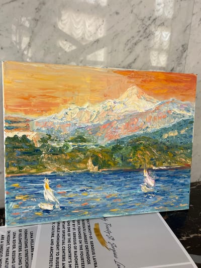 This media file features an oil painting with a thick impasto technique, depicting a dynamic seascape. The left side of the painting shows a warm, sandy beach with hues of orange and yellow. Transitioning to the right, the painting shifts to vibrant greens representing foliage or land, and finally to a deep blue sea, rendered with energetic brushstrokes. Two white birds with yellow accents are painted in flight over the water. The painting is displayed on a marbled surface, likely a table or floor, with shadows suggesting overhead lighting. To the right of the painting, a printed informational card is partially visible. The text on the card includes references to "HOLY TRINITY-ST. SERGIUS LAVRA," "RUSSIA'S LARGEST ORTHODOX," and "LENA PILLARS," indicating the painting may be related to Russian culture or landmarks. The overall impression is one of vibrant natural beauty and artistic expression. The setting in Geneva, Switzerland is noted.
