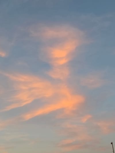 The image shows a light blue sky with orange clouds. The clouds are concentrated in the center and right of the image, appearing wispy and layered. A dark object is visible in the upper right corner. The image is rotated, and no information suggests its location is Hurghada, Egypt. There are no people visible.