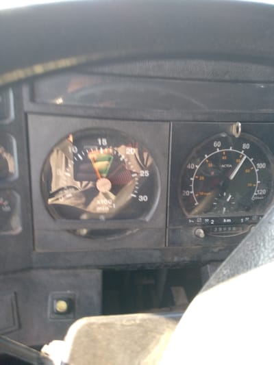 The image shows a close-up view of a truck's dashboard, located in Batpaktinskoe, Kazakhstan. The dashboard features two primary gauges: a tachometer on the left and a speedometer on the right. The tachometer, with markings up to 30 and labeled "x100 /min", shows the needle pointing between 10 and 15, in the green zone. The speedometer, with markings up to 120 and labeled "km/h", indicates a speed of approximately 50 km/h. Below the speedometer, an odometer displays the reading "39998". The dashboard is made of dark, textured plastic and appears to be aged. The lighting suggests it is daytime, with sunlight reflecting off some surfaces. There are no people visible in the image.