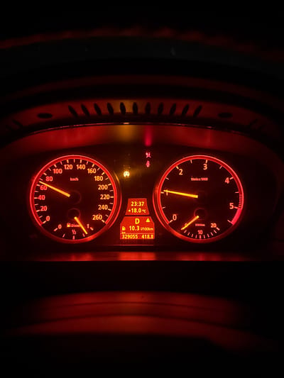 The image shows the illuminated dashboard of a car. The speedometer indicates a speed of approximately 80 km/h. The tachometer displays an engine speed around 1600 RPM. The fuel gauge reads approximately half full, and the display indicates "Diesel". The ambient temperature is +18.0°C. The current time is 23:37. The average fuel consumption is 10.3 l/100km. The odometer reads 329055 km, and the trip distance is 418.8. The transmission is in drive ("D"). The image was taken in darkness, and the location, Mogila, Bulgaria, is not evident in the image.