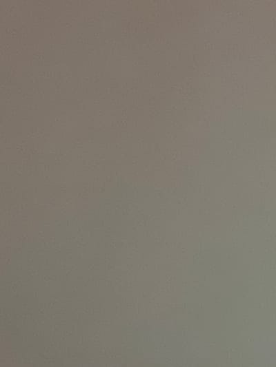 This is a full-frame, slightly desaturated, close-up, static shot of a neutral grey textured surface. The texture appears to be a fine, granular pattern with subtle variations in shade. There are no discernible subjects, objects, activities, or events taking place. The image provides no information about the time of day, weather, location cues, emotions, or any visible text. The image is likely a photograph of a wall, fabric, or similar surface.