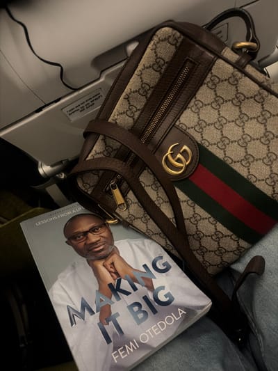 The image depicts a tan Gucci handbag with the brand's signature "GG" pattern and a green and red stripe. A book titled "Making It Big" by Femi Otedola rests next to the bag. The setting appears to be an airplane cabin, as evidenced by the armrest and seatbelt sign in the background. The exact location within Addis Ababa, Ethiopia, cannot be determined from the given information.