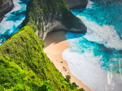 The image shows an aerial view of a tropical beach with turquoise water and white waves crashing against a sandy shore. Lush green vegetation covers the cliffs surrounding the beach. There are no indications that this image is in Basingstoke and Deane, United Kingdom.