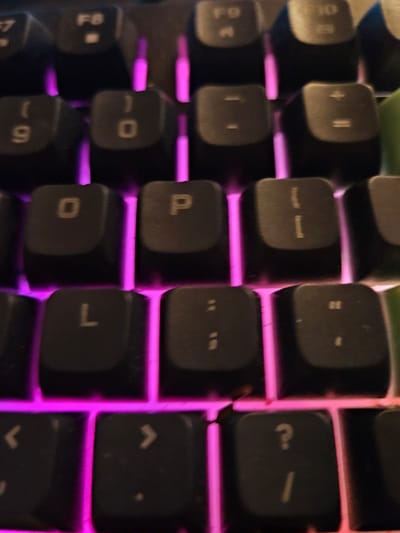 The image is a close-up, overhead view of a black mechanical keyboard with purple backlighting. The keys visible include F7, F8, F9, F10, 9, 0, -, =, O, P, [, ], L, ;, ,, ', and ?. The keyboard appears to be in good condition, with no visible damage. The image does not provide any information about the location in the city of Versailles, France, or any people, actions, interactions, or environmental details outside of the keyboard itself.