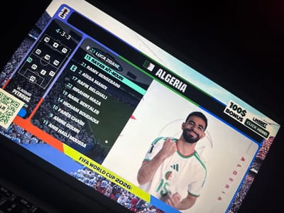 The image shows a laptop screen displaying a sports-related graphic. The graphic features a football formation diagram labeled "4-3-3" and a list of players with numbers, including "23 LUCA ZIDANE," "15 RAVAN AIT-NOURI," and "19 NABIL BENETALEB." The flag of Algeria is visible, along with the text "ALGERIA." A player in an Algerian jersey is prominently featured on the right side of the screen. There is also an advertisement banner at the top right corner that reads "100$ BONUS LINEBET CLICK HERE!". The bottom of the screen displays "FIFA WORLD CUP 2026". The scene is viewed from an angle, with the laptop on a dark surface, possibly a table, and a black keyboard is partially visible. The background of the graphic shows a crowd of spectators. There is no indication of the city of Kufena, Nigeria in the image.