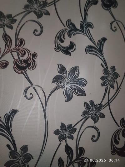 The image shows a close-up of wallpaper with a floral, vine-like pattern. The pattern features stylized flowers and swirling leaves in dark gray and black, with some accents that appear to be metallic or glittery. The background of the wallpaper is a textured off-white or light beige. The image contains a timestamp in the bottom right corner: "21.06.2026 06:14". There are no people or specific identifiable locations within the image itself. The description of Zarafshan City, Uzbekistan, is not present in the visual data of the image.