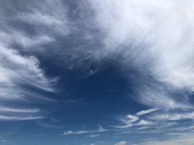 This is a photograph of a dynamic sky with a mix of wispy cirrus clouds and denser formations. The sky transitions from a deep, rich blue in the lower half to a lighter blue and white in the upper half, where the clouds are more prominent. The clouds are streaky and feathery, suggesting movement and wind.

In the upper left quadrant, a small, dark object is visible against the sky, which appears to be a drone or a small aircraft. It is a solitary object in the vast expanse of the sky.

The lighting suggests it is daytime, likely mid-morning or afternoon, as there are bright white areas in the clouds, indicating sunlight. The overall impression is one of a bright, breezy day. The location context is Barrie, Canada. There is no visible text in the image.