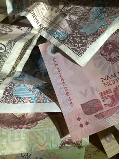 Close-up of Vietnamese Dong currency, specifically 50,000 VND notes, partially visible and piled together. The scene is likely located in Sà Phìn Commune, Vietnam.