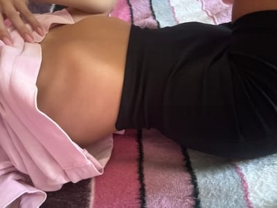 An overhead shot shows a person lying down, draped in a pink garment on their left and wearing black on their right. They are positioned on a striped blanket, with colors of pink, white, and black. The person's midsection and a portion of their legs are visible. The lighting suggests a casual indoor setting. The image does not provide any contextual information that would allow for identifying a specific location within Basarabeasca, Moldova.