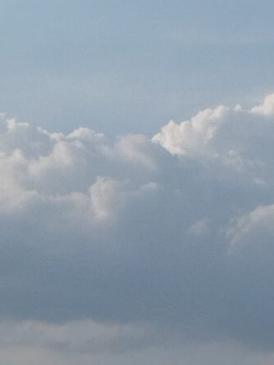 This is a vertical, medium shot of a cloudy sky. The sky is a pale blue, with the clouds appearing white and gray. The clouds are fluffy and appear to be moving across the sky. The image seems to be taken on a bright day, possibly during the day. The overall impression is one of a vast, open sky, with the clouds creating a sense of depth and texture. The image is likely a landscape shot focused on the sky. There is no visible text in the image.