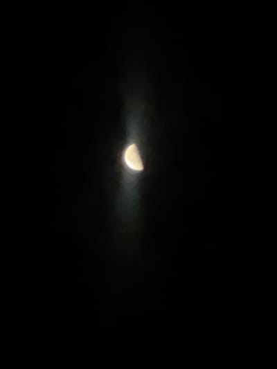 The image shows a half-moon in a dark sky. There is some atmospheric haze or light pollution around the moon, giving it a slightly diffused appearance and a light yellow glow. The rest of the image is black, indicating a nighttime scene. The image does not contain any elements that would suggest a specific location in Mlada Gvardia, Bulgaria, or any people, actions, or interactions. It is a simple celestial photograph.