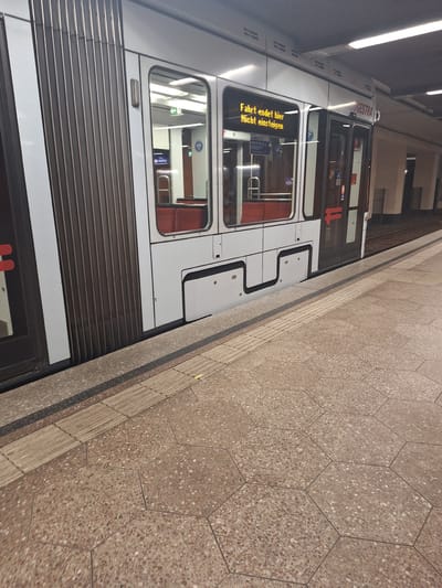 The image depicts a tram at a station in Bochum, Germany. The tram, with its white exterior and dark ribbed doors, is stationary at the platform. A digital display on the tram window shows text in German: "Fahrt endet hier. Nicht einsteigen." (Journey ends here. Do not board.) The platform is paved with hexagonal, speckled tiles. Tactile paving, designed for visually impaired individuals, runs along the edge of the platform. The environment appears to be an indoor or covered station, with artificial lighting illuminating the scene. No people are visible in the immediate vicinity of the tram doors, though the interior of the tram shows red seating. The name "BOGESTRA" is visible on the upper part of the tram, which is the public transport operator for the Ruhr area, including Bochum.