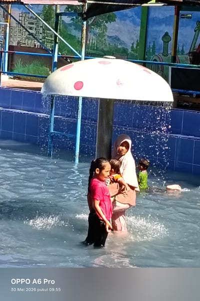 The image shows a group of people in a swimming pool. A woman wearing a hijab is standing in the water with two children. Another child in a green shirt is also in the water nearby. A mushroom-shaped sprinkler is above them, dispensing water. The pool has blue tiled walls. In the background, there are painted murals of buildings and landscapes. The image includes a watermark "OPPO A6 Pro" and the date "30 Mei 2026 pukul 09.55." It is located in Palohseulimeng, Indonesia.