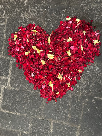 A heart shape formed from red and yellow rose petals rests on a dark grey stone surface in Huejotzingo, Mexico. The stone appears to be a walkway or patio, with visible grout lines and a rough texture. The rose petals are scattered loosely within the heart shape, with some individual petals falling outside the boundary. The lighting is even, casting no distinct shadows, suggesting an overcast day or indirect light source. There are no people or other objects present in the frame.