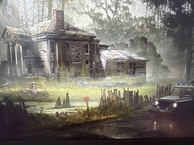 The media file depicts a desolate and overgrown scene featuring a dilapidated mansion. The mansion, with its broken windows and weathered facade, is surrounded by dense, misty woodland and tall grass. Several objects are scattered around the property, including a rusty, unidentified piece of machinery partially obscured by vegetation and a rough wooden fence. A small, weathered sign with visible text is planted in the ground near the fence. In the foreground, a dark, off-road vehicle with its headlights on is partially visible, positioned on a muddy track that appears to have puddles. The overall atmosphere is eerie and post-apocalyptic, suggesting abandonment and decay. The time of day appears to be either dawn or dusk, with the lighting creating a hazy and atmospheric effect. The location cues suggest a rural or wilderness setting, possibly in a swampy or humid environment given the overgrowth and mist. No people are visible in the scene. The visible text on the sign appears to read "NO TRESPASSING".