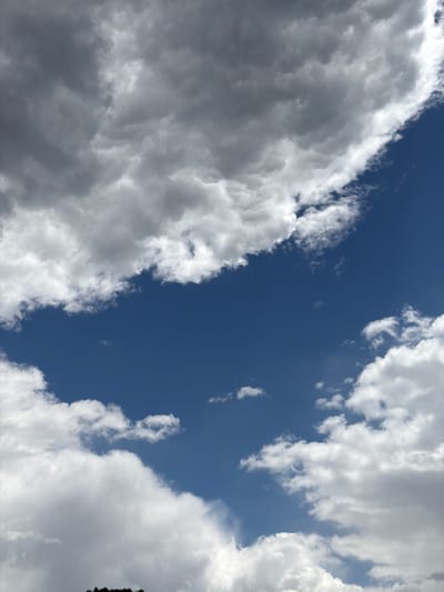 The image shows a view of the sky with cumulus clouds. A patch of deep blue sky is visible between the clouds. The clouds on the left side of the image are darker, suggesting heavier moisture content. The image does not provide any information about the location or city. No people, subjects, objects, actions, or interactions are visible.