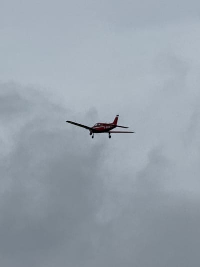 A red and black biplane is flying upside down in a cloudy sky. The location is likely near Epping Forest, United Kingdom, based on the prompt. There are no visible people.