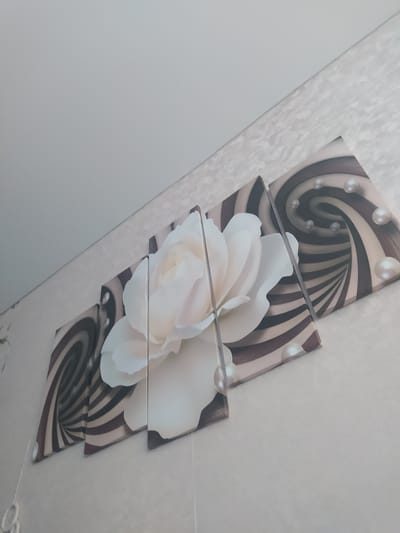 The image shows a four-panel canvas art piece hanging on a textured, light-colored wall. The artwork features a large, white rose in the center, with swirling, abstract patterns in shades of brown and beige on the outer panels. Several pearls are depicted scattered across the artwork, some appearing to be embedded within the swirling patterns. The room appears to be an indoor setting, possibly a home, with a plain white ceiling visible at the top left of the image. The specific location of Gusev, Russia is not discernible from the visual information provided in the image.
