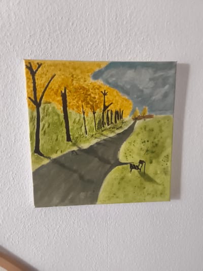 The image depicts a painting of a pathway winding through a grassy area lined with trees. The trees on the left have vibrant yellow foliage, suggesting autumn, while the sky on the right is a mix of grey and blue. A dark, winding path dominates the foreground, casting shadows onto the green grassy expanse. In the middle ground, to the right of the path, is a dark silhouette of a bench with a shadow extending from it. Further in the distance, a small building or structure with a yellowish roof is visible amidst a cluster of trees. The painting is mounted on a textured white wall. There is no indication of the city of Eitorf, Germany in the image.