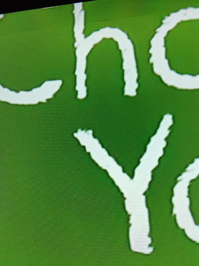 The image is a close-up of white lettering on a green background. The letters appear to be part of a phrase or word, with the visible parts showing "ho" and "YO". The lettering is stylized and slightly blurred, suggesting it is a photograph of a screen or display. The green background has a textured appearance, possibly indicating a fabric or a digital screen. There is no visible indication of the city of Merbopuntong, Indonesia, in the image. The image is purely a visual depiction of text.