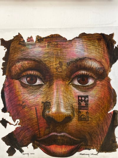 This image captures a mixed-media artwork, a portrait of a human face, located in Ikate, Nigeria. The artwork features a stylized face, appearing to be that of an African woman, constructed from a collage of torn paper segments bearing visible text and patterns, overlaid with drawing and paint. The complexion is rendered in earthy tones of brown, orange, and red, exhibiting a textured surface from fine lines. The subject's dark brown eyes gaze directly forward. A thin, dark vertical line is present on the viewer's left cheek. On the viewer's right cheek, a rectangular motif displays a checkerboard pattern atop a silhouette resembling a building. The edges of the portrait are irregular and jagged, set against a plain white background. Signatures "Razaq 2022" and "Abdulrazaq Ahmed." are visible at the bottom of the artwork.