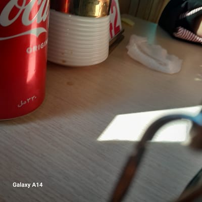The image shows a partially visible can of Coca-Cola, along with a white disposable cup with ridges. There's also a napkin or tissue present. The location is identified as Al-Mawasi, but no further details about people, subjects, objects, actions, interactions, or specific environment elements beyond what's immediately visible are discernible.