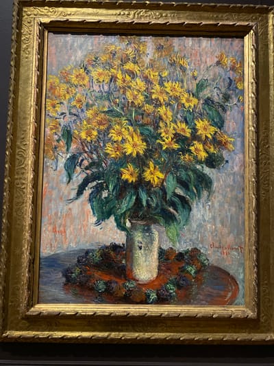 This is an oil painting on canvas by Claude Monet, titled "Sunflowers". The painting depicts a vibrant bouquet of sunflowers arranged in a vase, with a backdrop of brickwork. The sunflowers are rendered in bold brushstrokes, with shades of yellow and orange dominating the composition. The foliage is a mix of deep green and darker hues, suggesting depth and form. To the right of the sunflowers, a portion of a terracotta-colored urn or architectural element is visible, adorned with dark green and deep purple accents that could be other flowers or foliage. The background is a textured expanse of brickwork, rendered in pinks, grays, and blues, creating a soft, diffused light. The painting appears to be signed "Claude Monet" and dated "1880" in red script on the upper right quadrant of the canvas. The artwork is housed in an ornate, gilded frame. The scene evokes a sense of abundance and the beauty of nature, typical of Monet's Impressionist style, with the bright sunflowers radiating warmth and life. The time of day and weather are not explicitly depicted, but the diffused light suggests an ambient, possibly overcast or diffused sunlight. The painting is located in Washington, United States of America.