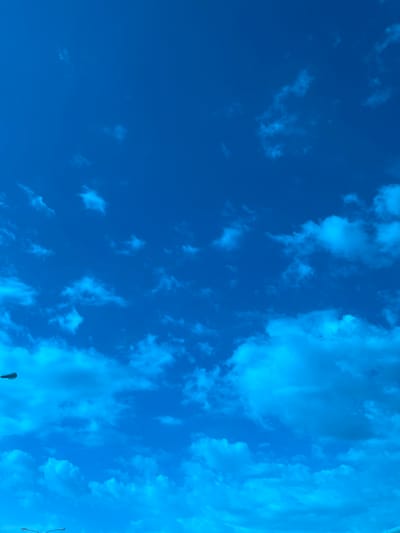 The image shows a bright blue sky with scattered clouds. The clouds range in density and shape, with some appearing as thin, wispy streaks and others as larger, more defined formations. The sky is clearest in the lower left portion of the frame. A lamppost is visible near the bottom of the frame. The photograph was taken in Tlustenkhabl, Russia.