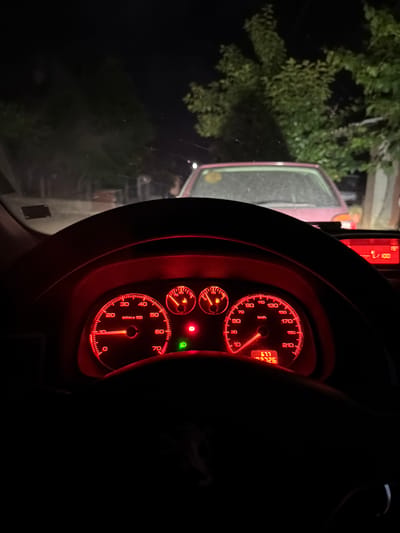 The image shows the dashboard of a vehicle at night. The dashboard has red lighting. The speedometer reads approximately 10 kilometers per hour, and the tachometer reads approximately 0 RPM. The odometer reads 92,726 kilometers. Through the windshield, a red vehicle is visible, and trees are visible in the dark background. There is no information provided in the image to determine the location is in Parvomai, Bulgaria.