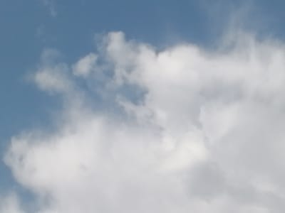 The image depicts a close-up view of a blue sky filled with fluffy white clouds. The clouds are varied in size and density, with some appearing wispy and translucent while others are thick and opaque. There are no discernible landmarks or structures visible, suggesting the image was taken from an open area. The lighting appears to be natural daylight, casting soft shadows on the clouds. The scene is devoid of any human presence, animals, or man-made objects. The image is purely a natural landscape of the sky and clouds. The location in Gumbaz, Uzbekistan, is not visually identifiable from the image itself.