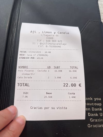 The image shows a receipt from a restaurant called Ají, Limón y Canela, located at C/Sagasta 66, 35008, Las Palmas de Gran Canaria, Spain. The coordinates provided place the restaurant in the neighborhood of Triana in the city of Las Palmas. The receipt details an order of one Ceviche for 16.00€ and two Caña Dorada for 6.00€, totaling 22.00€. The receipt was issued on 17/04/2025 at 16:48 to a table labeled "Mesa 17 (Terraza)" and was served by a person named "Wilma". The receipt also displays the restaurant's phone number, 928 909 621, Instagram account, @ajilimonycanelagc, and tax identification number, B-76306646. The receipt also shows the breakdown of the total amount, including the base price of 20.56€ and the VAT (IGIC) of 7.0%, which amounts to 1.44€. Finally, the receipt includes a thank you message in Spanish, English, French, German, and Italian. The receipt is held by a hand, obscuring part of the bottom.