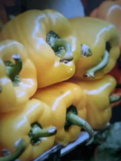 The image showcases several vibrant yellow bell peppers, closely packed together. Each pepper displays a glossy surface and a prominent green stem. The arrangement creates a cluster, with some peppers partially obscured by others. The background is blurred, highlighting the peppers as the focal point. The overall impression is fresh and visually appealing, emphasizing the natural beauty of the produce.