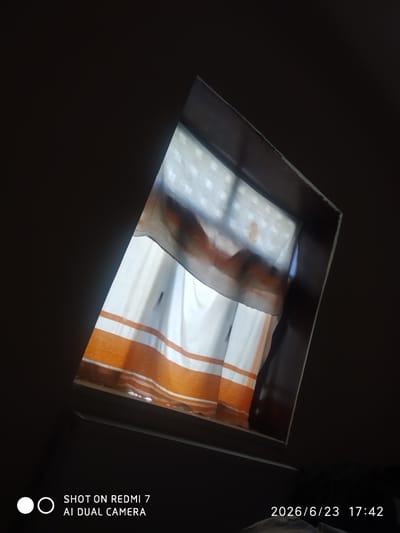 The image shows a view looking up into a dark ceiling with a rectangular opening revealing a window with white and orange striped curtains. The opening is framed by what appears to be dark wood. The lower portion of the image contains text overlay that reads "SHOT ON REDMI 7 AI DUAL CAMERA" and a date and time stamp "2026/6/23 17:42". There is no discernible information about the city of Khalkabad, Uzbekistan, or any specific people, actions, or interactions.
