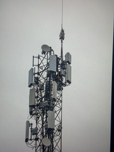 The media file is a photograph of a telecommunications tower with multiple antennas and equipment attached. The tower structure is a complex lattice of metal beams. Various rectangular and circular antennas, along with associated wiring and mounting hardware, are visible. The background is a plain, light-colored surface, possibly the sky, with a subtle grid pattern suggesting a digital display. The image is taken from a distance, showing a portion of the tower extending horizontally across the frame. No people are visible, and the overall impression is of an industrial or infrastructure-related scene. The lighting suggests it might be daytime, but no specific time of day or weather conditions can be determined from the image alone. There are no discernible location cues within the image itself, other than the provided context of Eyüpsultan, Turkey. There is no visible text.