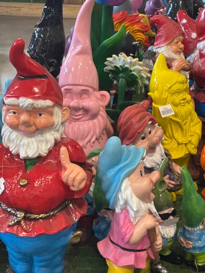 A high-angle, full-frame shot depicts a pile of vibrantly colored garden gnomes. The gnomes are of various sizes, poses, and colors, including red, yellow, green, blue, pink, and black. Some are wearing hats, holding tools, or have other decorative elements. The gnomes are densely packed together.

Based on the metadata, this image was taken in Mouscron, Belgium.