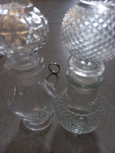 The image shows two textured glass bottles lying horizontally on a mottled gray surface. A silver ring rests between the necks of the bottles. The scene is indoors with indirect lighting. There is no information within the image to place this scene in Trujillo, Peru.