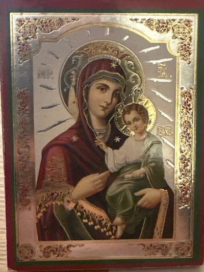 This is a close-up, horizontally oriented photograph of an Eastern Orthodox icon, likely depicting the Virgin Mary and the Christ Child. The icon is framed by a decorative border with intricate golden scrollwork against a lighter background. The central figures are rendered with soft features and serene expressions. The Virgin Mary is shown in profile, gazing towards the viewer. She wears a deep red garment and a veil. Her head is surrounded by a halo, and a star is visible on her garment. The Christ Child is nestled in her arms, looking upwards with a gentle gaze. He is dressed in a white tunic and a green mantle. Both figures have halos, indicating their divine status.

The background of the icon is a pale, textured surface, possibly silver leaf, with stylized rays emanating from behind the halos. There are inscriptions in what appears to be Church Slavonic or Greek script. On the lower left, the letters "MP" are visible, likely an abbreviation for "Mater Dei" (Mother of God). Above the Christ Child, there are other inscriptions that are partially obscured but appear to be abbreviations related to the figures.

The icon is set within a frame that includes a dark red outer edge and a thinner green band between the icon and the red edge. The overall impression is one of reverence and spiritual devotion. There are no discernible clues about the time of day, weather, or specific location within Marten, Bulgaria, beyond it being the setting for this religious artifact.