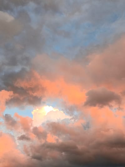 The image depicts a sky filled with a mixture of dark gray and vibrant pink and orange clouds, illuminated by what appears to be the setting sun. The clouds are dense and textured, with some areas appearing wispy and others thick and voluminous. Patches of light blue sky are visible between the clouds. The scene is a natural landscape, devoid of any man-made structures or human presence. There is no indication of the specific location in the city of Лосева, Belarus, as the image focuses solely on the sky.