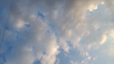 This media file depicts a view of the sky with clouds and overhead wires, suggesting an outdoor setting, possibly in Kryzhanivka, Ukraine. Several birds are visible in flight against the backdrop of a partly cloudy sky, indicating daytime. The lighting suggests it could be either early morning or late afternoon, as the sun's rays are illuminating some of the clouds with a warm, yellowish glow, while other parts of the sky are a clear blue. The presence of multiple wires, running diagonally across the frame, implies a connection to power or telecommunication infrastructure, common in populated areas. There are no people visible, and the focus is solely on the natural elements and man-made structures in the sky. The overall mood is tranquil, with the birds adding a dynamic element to the scene. No text is present in the image.