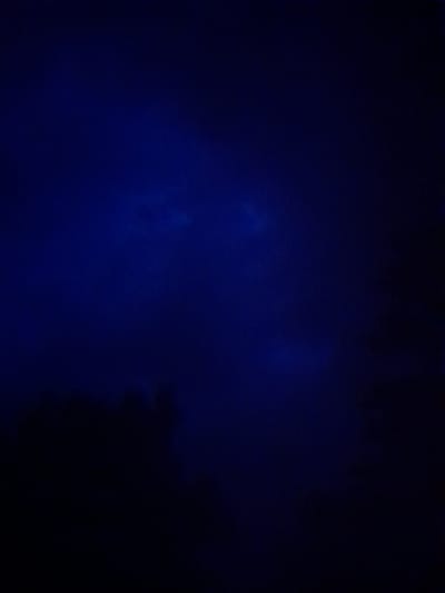 The image is a dark, abstract composition dominated by deep blues and blacks. It appears to be a photograph of an indistinct, possibly celestial or atmospheric, phenomenon. There are subtle lighter blue or white wispy forms scattered across the dark expanse, suggesting clouds, nebulae, or perhaps electrical discharges. The overall effect is one of depth and mystery, with the darkness implying a nighttime or deep-space setting. No specific objects, people, or discernible scenes are present. The lighting is extremely low, with only faint illuminated areas breaking through the overwhelming darkness. The textures appear somewhat grainy, characteristic of low-light photography. No text is visible in the image. The context of Kliushnykivka, Ukraine, does not provide any direct visual clues within the image itself, as the subject is abstract and lacks identifiable features of any specific location.