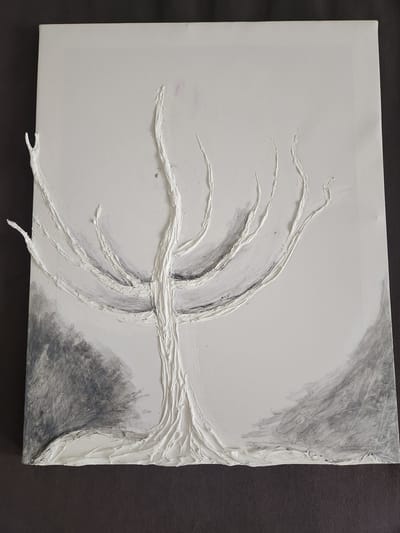 The image displays a close-up, overhead view of a textured painting on canvas. The artwork features a stark white, relief sculpture of a bare tree with gnarled branches. The tree's base and trunk are rendered with thick, impasto-like applications of white paint, creating a sense of ruggedness. The branches extend outwards across the canvas, thinning as they reach the edges. Some of the branches have small, twig-like extensions. The background is a subtle blend of off-white and grey, with darker, smudged grey areas suggesting foliage or ground cover on the left and right sides of the tree. The texture of the canvas is visible beneath the paint. The painting is presented against a dark grey, textured surface, likely a table or backdrop. The scene depicted is an artwork, and its location within the city of Vniissok, Russia, is not discernible from the image itself. There are no people, actions, or interactions visible.