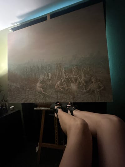 The image shows a large, detailed painting on an easel. The painting appears to depict a chaotic, perhaps war-torn scene with numerous figures and structures. The color palette is muted, dominated by browns, grays, and a dusty pinkish hue, suggesting a somber or historical subject. The figures in the painting are rendered in a realistic yet stylized manner, with some appearing to be engaged in manual labor or conflict.
In the foreground, the lower half of a person's legs and feet are visible. They are wearing open-toed black sandals with straps. The legs are illuminated by a light source that casts shadows, indicating the presence of artificial lighting in the room. The painting is positioned on a wooden easel, and behind it, the wall is painted a light green on the left and a dark teal on the right. The ceiling has a blueish-gray stripe, possibly from lighting or a decorative element.
The setting appears to be an indoor space, likely an artist's studio or a room where a large artwork is being displayed or worked on. The overall impression is one of an artistic endeavor in progress or a display of a significant artwork, with the artist or viewer's presence subtly indicated by their legs in the foreground. The image does not contain any identifiable landmarks or clues to pinpoint its location in Cape Coral, United States of America.