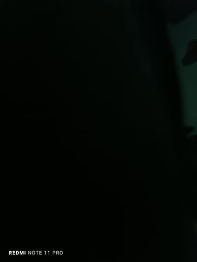 The image is a dark photograph, with the bottom left corner featuring the text "REDMI NOTE 11 PRO" in white font. The rest of the image is predominantly black, with a faint hint of a greenish hue in the upper right portion. There are no discernible people, subjects, or objects in the scene. The environment appears to be indoors and dimly lit. The location in Shopokov, Kyrgyzstan, is not visually represented in the image.