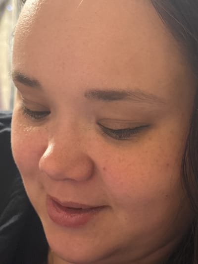 The image is a close-up, waist-up shot of a person's face. The person has brown hair, brown eyes, and light skin with freckles. They are wearing dark clothing. The lighting in the image is warm and soft, creating a gentle mood. The background is out of focus, but appears to be indoors, possibly a home environment. The image does not provide any information about the location in Tarasovka, Russia.