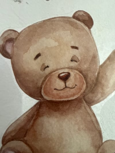 The image is a close-up watercolor painting of a cartoon teddy bear. The bear is light brown with darker brown accents on its ears, nose, and eyes. It has a round face with closed eyes, a small smile, and a reddish-brown nose. Its right arm is raised as if waving. The background is a plain, textured white. There is no discernible location in the city of Ushtobe, Kazakhstan, or any real-world environment depicted.
