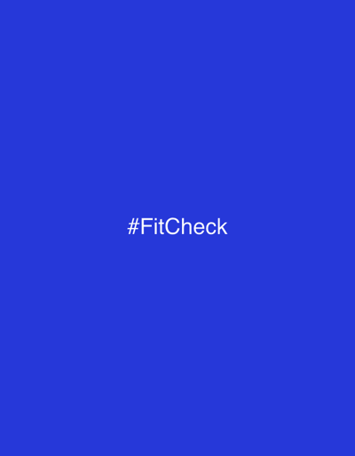 The image displays a plain, solid blue background. Centered horizontally and slightly above the vertical midpoint of the frame, the white text "#FitCheck" is prominently featured. There are no other subjects, objects, or activities depicted. The scene lacks specific location cues, weather, or time of day indicators, presenting a minimalist aesthetic. The image is set in the context of Zovuni, Armenia.