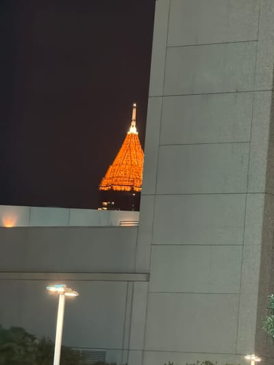 The image depicts the Tokyo Tower in Japan at night, viewed from an elevated position behind buildings. The tower is illuminated in orange light. A street lamp is also visible.