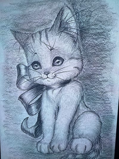 The image is a pencil sketch of a stylized kitten with large, expressive eyes and prominent whiskers. The kitten is seated and adorned with a large bow on its left side. The background is a textured wash of grey tones. There is no discernible location in Košice, Slovakia, as the image is an artwork and not a photograph of a real-world scene.