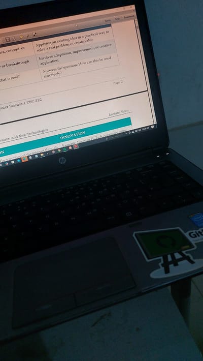 The image shows a close-up view of a laptop screen displaying a document. The document appears to be a lecture note, with headings such as "Lecture Notes", "INNOVATION", and text relating to "Computer Science | CSC 322". The laptop's keyboard and trackpad are visible below the screen. The overall lighting suggests the image was taken in a dimly lit indoor environment. There is no visible indication of the city of New Nyanya, Nigeria, or any other specific geographical location. The scene is static and focuses on the digital content on the laptop screen and the device itself.