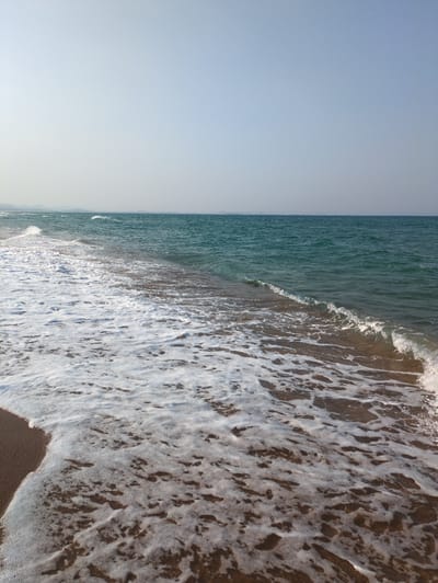 A sideways view shows a beach scene. On the left is a light blue sky. The water on the beach is a deeper blue-green color. White foam from the waves covers a portion of the water and the beach on the right. The location is Tuy Hoa, Vietnam.